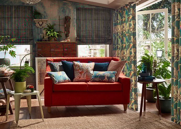 A bright botanical conservatory is shown with a ruby red sofa in the centre. The theme is tropical.